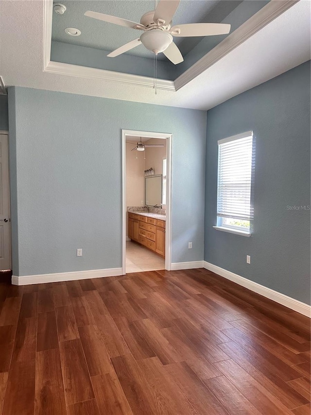 unfurnished bedroom with hardwood / wood-style floors, a raised ceiling, connected bathroom, and ceiling fan