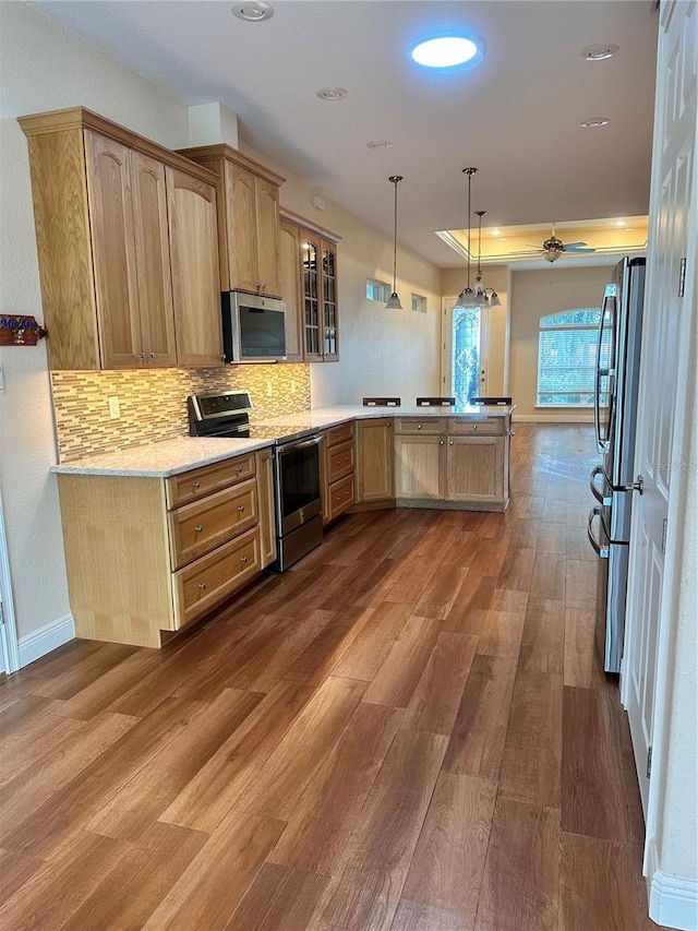 kitchen with appliances with stainless steel finishes, tasteful backsplash, wood-type flooring, kitchen peninsula, and ceiling fan