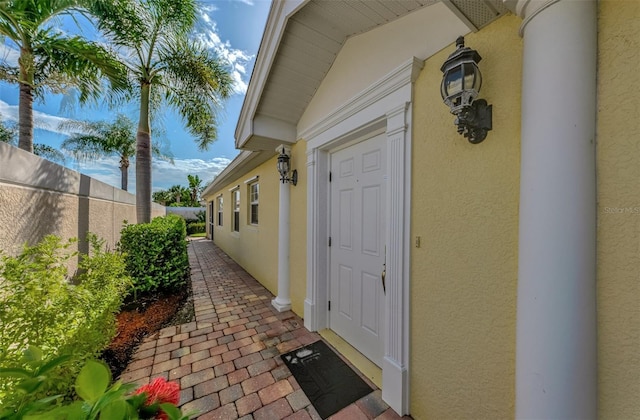 view of exterior entry with a patio area, fence, and stucco siding