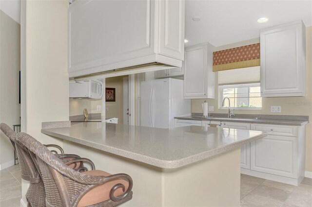 kitchen with a breakfast bar area, a peninsula, white appliances, white cabinets, and light countertops