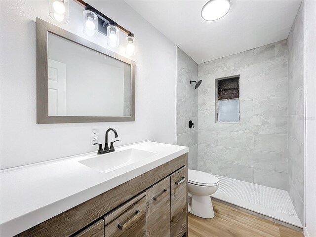 bathroom with toilet, a tile shower, hardwood / wood-style floors, and vanity