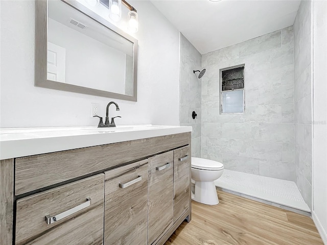 bathroom featuring a tile shower, toilet, vanity, and wood-type flooring