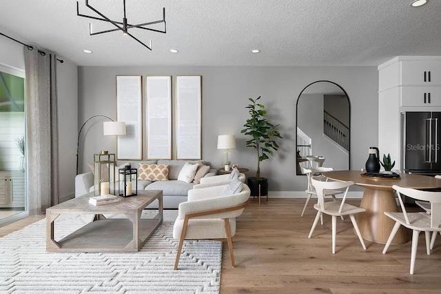 living room featuring light wood-type flooring, a notable chandelier, and a textured ceiling