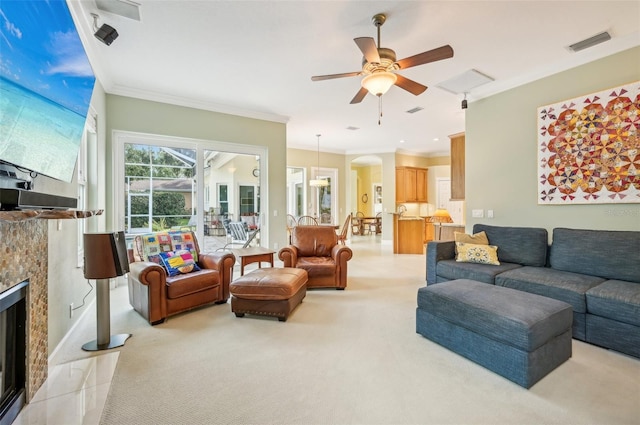 living room featuring ceiling fan, ornamental molding, light colored carpet, and a tile fireplace