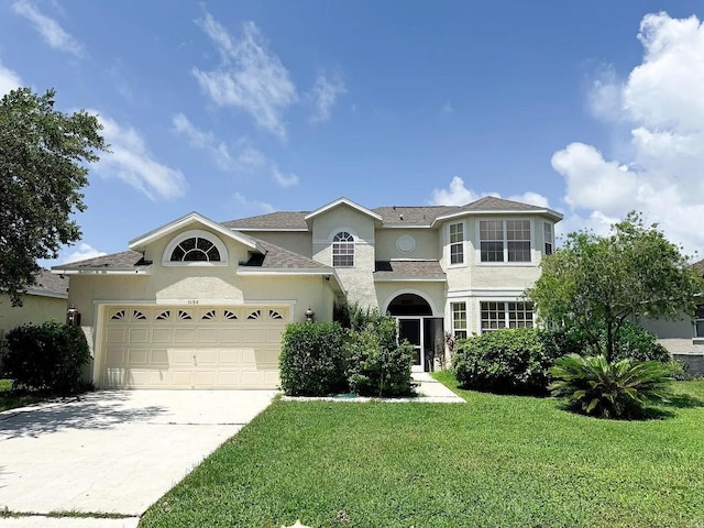 traditional-style house with a garage, concrete driveway, a front yard, and stucco siding