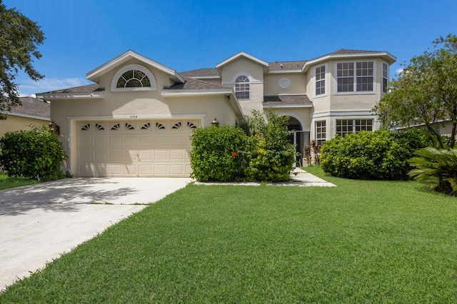 traditional-style house featuring a garage, driveway, a front yard, and stucco siding