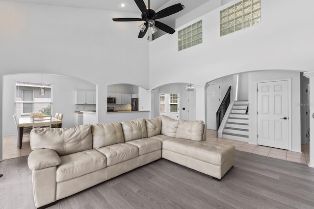 living area featuring arched walkways, a ceiling fan, stairway, light wood-type flooring, and ornate columns