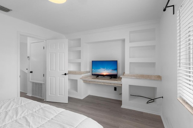 bedroom with wood finished floors, built in study area, visible vents, and baseboards