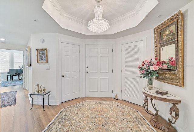 entryway featuring a tray ceiling, hardwood / wood-style flooring, crown molding, and a notable chandelier