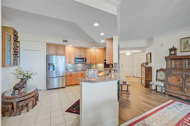 kitchen with light hardwood / wood-style flooring, stainless steel appliances, kitchen peninsula, light stone countertops, and vaulted ceiling