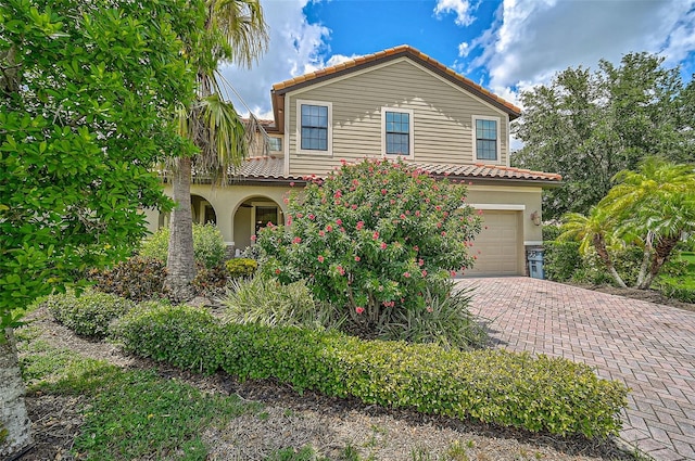 mediterranean / spanish-style house with a tile roof, decorative driveway, an attached garage, and stucco siding