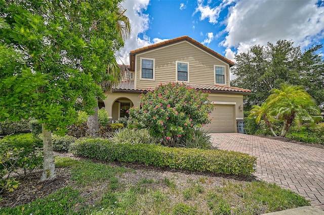 mediterranean / spanish-style house featuring stucco siding, an attached garage, a tile roof, and decorative driveway