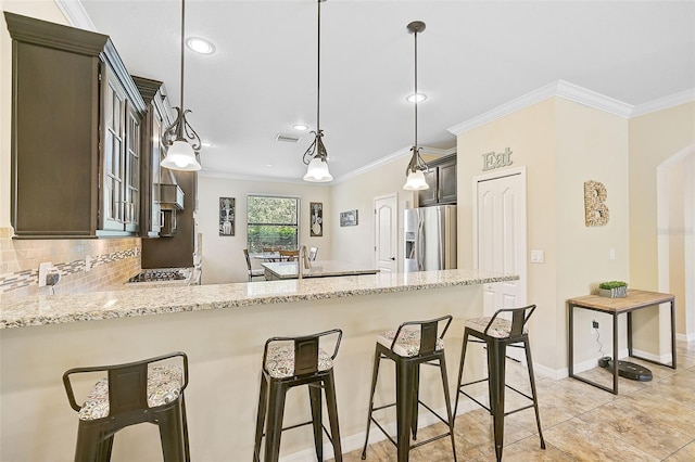 kitchen featuring light stone counters, a breakfast bar, stainless steel refrigerator with ice dispenser, crown molding, and backsplash