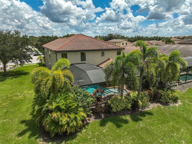 rear view of property with a yard, stucco siding, glass enclosure, and a tile roof