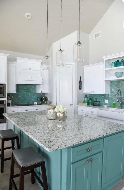 kitchen featuring backsplash, appliances with stainless steel finishes, a kitchen island, white cabinetry, and lofted ceiling