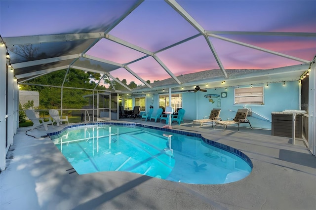 pool at dusk with a lanai, ceiling fan, and a patio