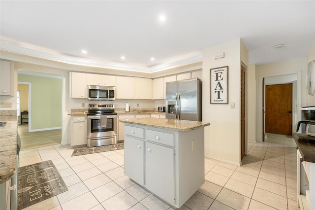 kitchen featuring light tile patterned floors, a center island, appliances with stainless steel finishes, light stone countertops, and ornamental molding