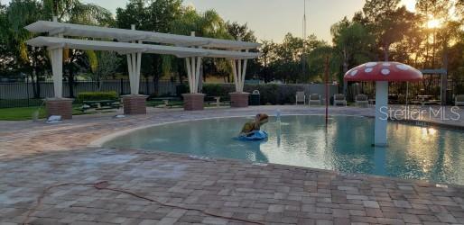 pool at dusk featuring a patio area and a pergola