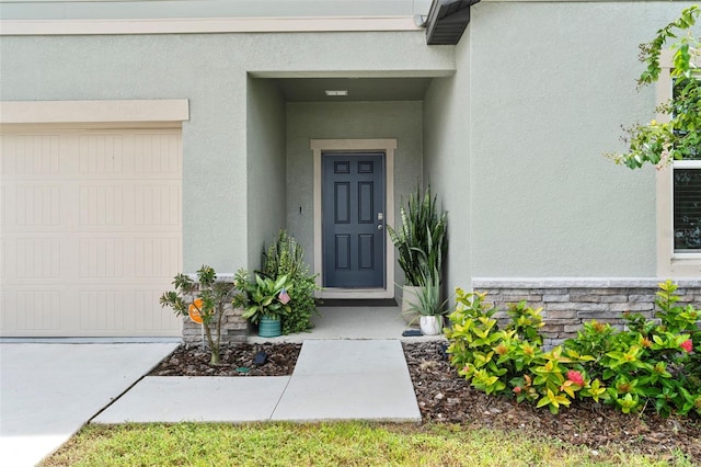 view of exterior entry featuring an attached garage, stone siding, and stucco siding