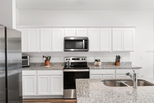 kitchen with light stone counters, wood finished floors, a sink, white cabinetry, and appliances with stainless steel finishes