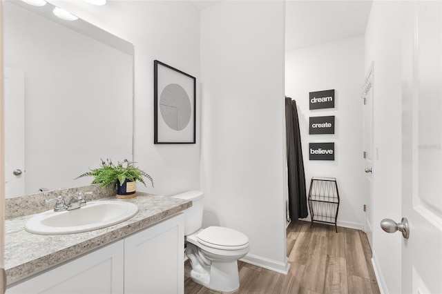 bathroom featuring toilet, baseboards, wood finished floors, and vanity