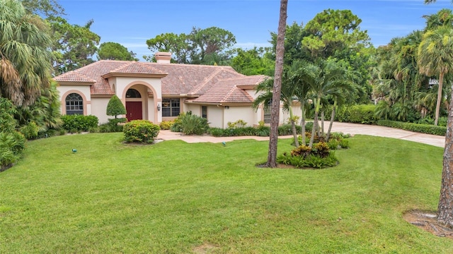 mediterranean / spanish home with a front yard, driveway, stucco siding, a chimney, and a tile roof