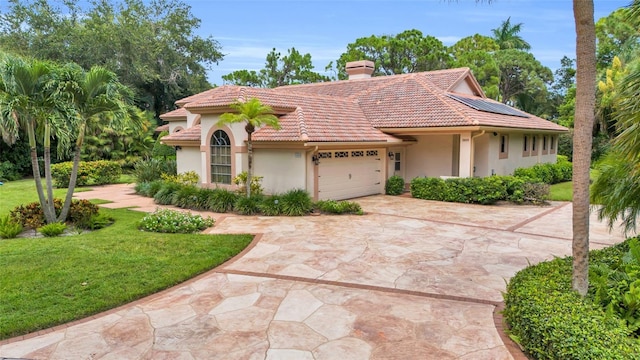 view of front of property featuring an attached garage, driveway, a tiled roof, a front lawn, and a chimney