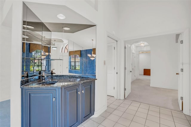 kitchen with light carpet, blue cabinets, dark stone counters, sink, and decorative light fixtures