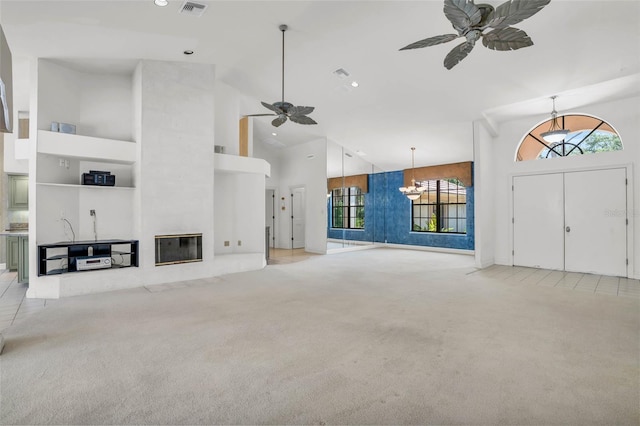 unfurnished living room with light colored carpet, high vaulted ceiling, a wealth of natural light, and ceiling fan with notable chandelier