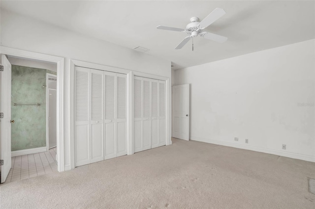 unfurnished bedroom featuring light carpet, multiple closets, and ceiling fan