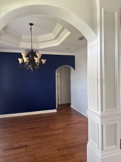 spare room with dark hardwood / wood-style floors, a raised ceiling, a notable chandelier, and ornamental molding