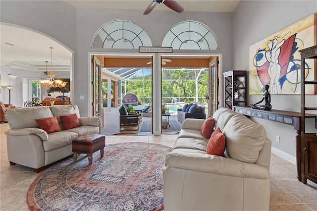 living room with arched walkways, a sunroom, tile patterned flooring, baseboards, and ceiling fan with notable chandelier