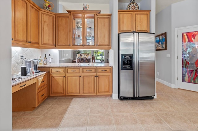 kitchen with light stone counters, light tile patterned flooring, backsplash, brown cabinets, and stainless steel fridge