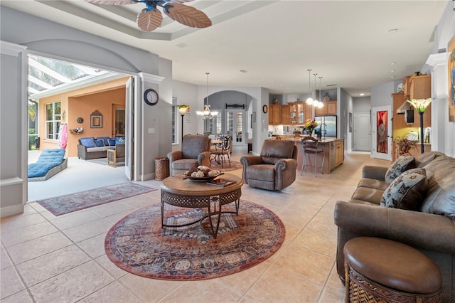 living area with light tile patterned floors, baseboards, and ceiling fan with notable chandelier