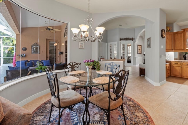 dining area featuring light tile patterned floors, ceiling fan with notable chandelier, arched walkways, and baseboards