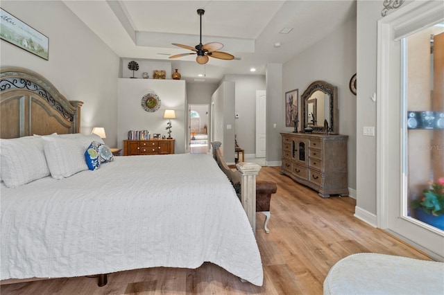 bedroom featuring recessed lighting, a ceiling fan, baseboards, light wood-type flooring, and a tray ceiling