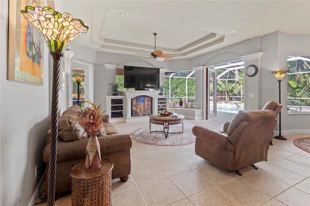 living area with ceiling fan, a tray ceiling, light tile patterned flooring, and a sunroom