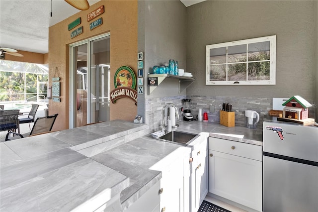 kitchen with tasteful backsplash, white cabinets, a ceiling fan, freestanding refrigerator, and a sink