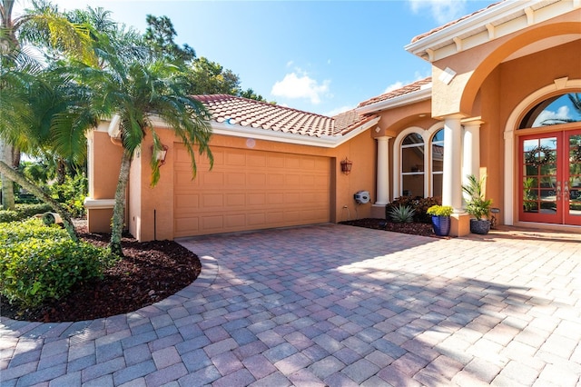 view of front of home featuring an attached garage, stucco siding, decorative driveway, and french doors