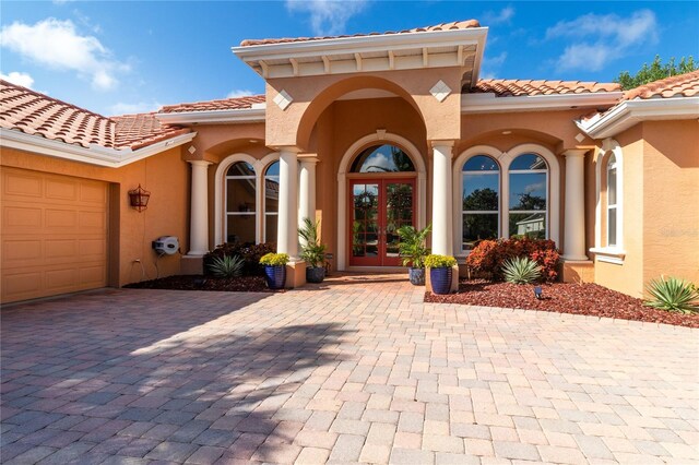 view of exterior entry featuring french doors, decorative driveway, stucco siding, a garage, and a tiled roof