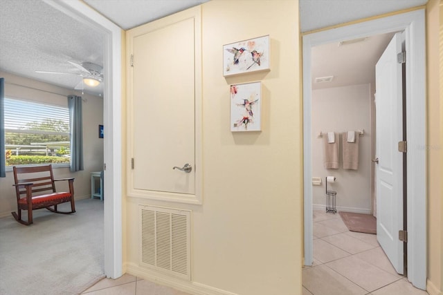 hall with light tile patterned floors, visible vents, a textured ceiling, and light colored carpet