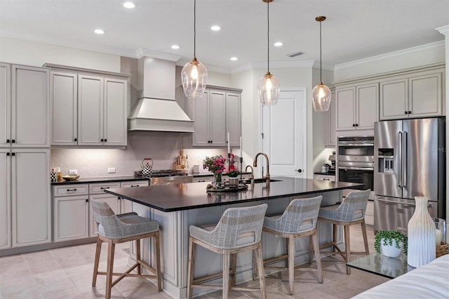 kitchen featuring gray cabinets, custom exhaust hood, stainless steel appliances, an island with sink, and hanging light fixtures