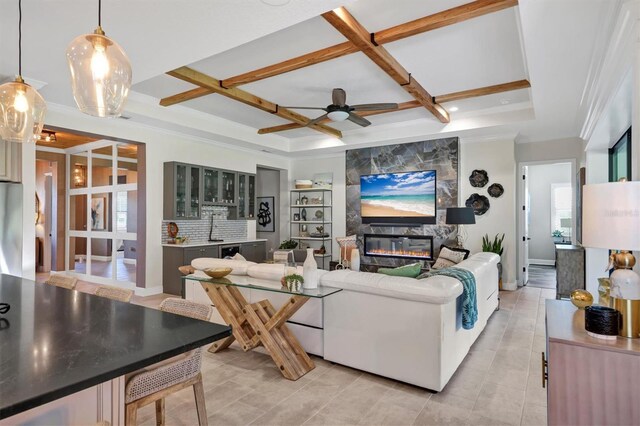 living room with coffered ceiling, a healthy amount of sunlight, a premium fireplace, ceiling fan, and beam ceiling