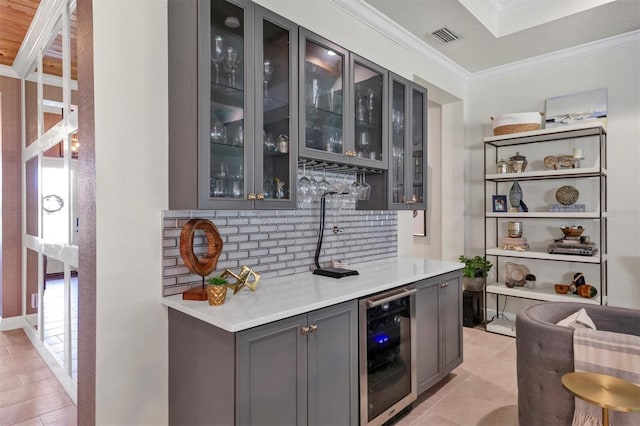 bar with crown molding, tasteful backsplash, beverage cooler, gray cabinetry, and light tile patterned flooring