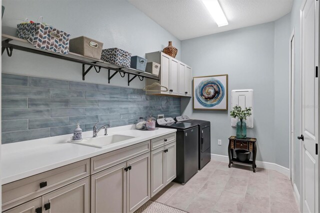 clothes washing area featuring cabinets, a textured ceiling, washing machine and dryer, sink, and light tile patterned flooring