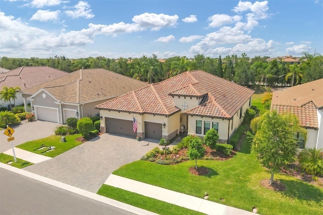 mediterranean / spanish home with decorative driveway, a tile roof, an attached garage, stone siding, and a front lawn