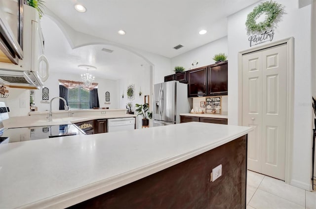 kitchen featuring dark brown cabinetry, dishwasher, light tile patterned floors, kitchen peninsula, and stainless steel fridge