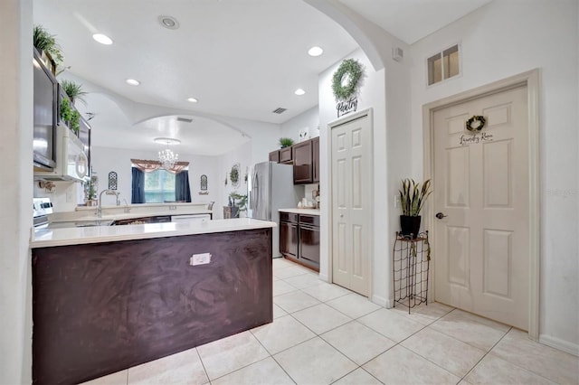 kitchen featuring dark brown cabinets, kitchen peninsula, stainless steel fridge, and light tile patterned floors