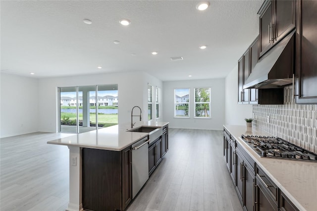 kitchen featuring under cabinet range hood, stainless steel appliances, a sink, and open floor plan