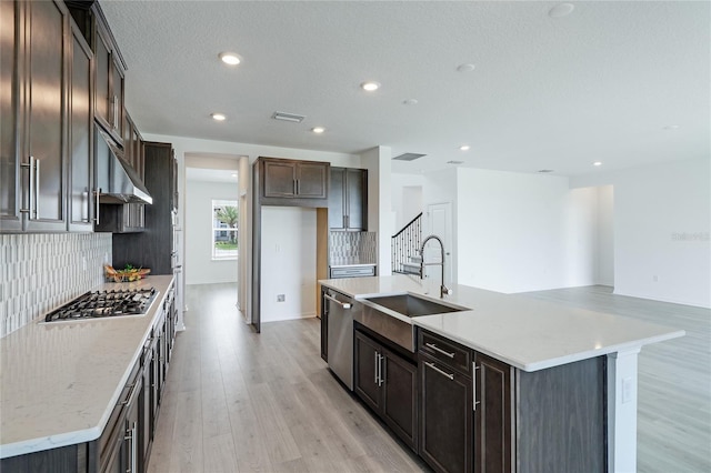 kitchen with range hood, light wood finished floors, stainless steel appliances, visible vents, and a sink